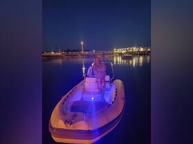 A man stands on a boat illuminated by soft lights at night, with a scenic dock and other boats in the background, creating a serene atmosphere perfect for evening outings.