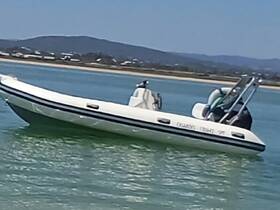 A sleek speedboat glides through calm waters, showcasing its design against a scenic backdrop of hills and shoreline.