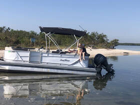 Two children enjoy a relaxing moment on a pontoon boat near a sandy beach, perfect for family outings and fun in the sun.