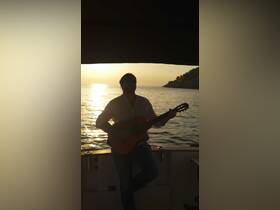 A musician plays guitar on a boat during a stunning sunset, creating a perfect ambiance for a memorable evening on the water.