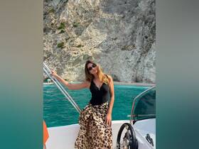 A woman poses on a boat with stunning rocky cliffs and turquoise waters in the background, capturing a perfect moment of relaxation and adventure on the water.