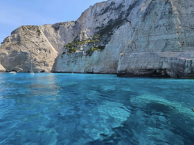 A stunning view of rocky cliffs rising above crystal-clear turquoise waters, showcasing the natural beauty of the coastline — perfect for exploring by boat.