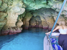 A stunning view of a woman exploring a cave by boat, surrounded by vibrant blue waters and rocky formations — a perfect adventure for nature lovers.
