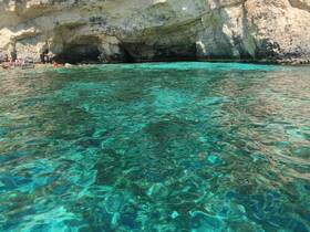 A stunning view of crystal-clear waters and a rocky coastline, with people enjoying the serene environment — perfect for beach lovers and adventure seekers.