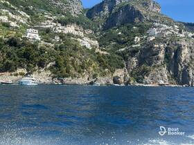 A stunning view of the Amalfi Coast featuring a yacht anchored near the rocky shoreline, showcasing the beautiful coastal scenery and lush greenery.
