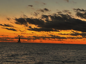 A serene sunset view featuring a sailboat silhouetted against a vibrant orange sky, perfect for capturing the beauty of evening sails.