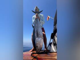 A proud angler holds up a large tuna catch on the deck of a boat, showcasing the thrill of deep-sea fishing in clear ocean waters.