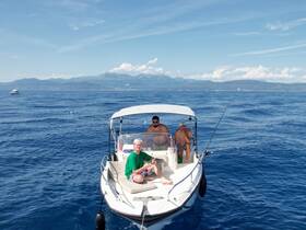 A group of friends enjoys a fishing trip on a boat in the open ocean, surrounded by stunning blue waters and distant mountains.