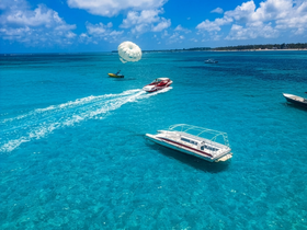 A vibrant scene showcasing parasailing over stunning turquoise waters, with multiple boats navigating the beautiful coastline — perfect for adventure seekers and water sports enthusiasts.
