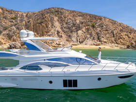 A stylish yacht glides through clear waters with a scenic beach backdrop, featuring a person enjoying the sun on deck — perfect for luxury cruising experiences.