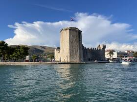 A picturesque view of a historic castle by the waterfront, with visitors enjoying the scenery — a perfect spot for sightseeing and boat tours.