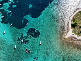A stunning aerial view of multiple boats scattered across vibrant turquoise waters, showcasing the beauty of a coastal paradise.