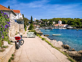 A scenic view of a coastal path in Maslinica, featuring a bicycle and picturesque waterfront homes, ideal for exploring the charming seaside village.