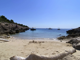 A picturesque beach scene featuring a rocky coastline and boats anchored in the clear blue waters, perfect for a relaxing day by the sea.