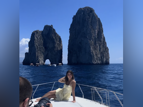 A woman poses on the bow of a boat with stunning rock formations in the background, capturing a perfect moment of adventure and exploration in beautiful waters.