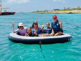 A joyful group of family members enjoys a sunny day on the water, relaxing in an inflatable boat while waving and having fun in the turquoise sea.