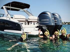 A joyful group of snorkelers, including children, wave from the water next to a Regal boat, showcasing a fun family adventure on the water.
