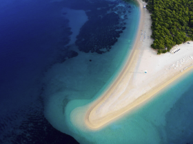 A stunning aerial view of a picturesque beach with a curved shoreline, showcasing the vibrant colors of the water and lush greenery — an ideal destination for relaxation and exploration.