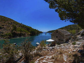 A picturesque view of a tranquil harbor surrounded by lush hills and a charming stone house, perfect for exploring the beauty of nature and enjoying peaceful boating experiences.