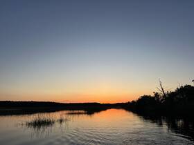 A serene sunset over a tranquil waterway, reflecting vibrant colors and surrounded by lush greenery — perfect for peaceful evening cruises.