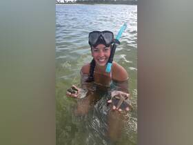 A snorkeler joyfully holds a starfish and a shell while wading in shallow waters, showcasing a delightful moment of human-animal interaction in a vibrant marine environment.