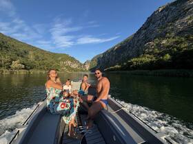 A joyful family enjoys a scenic boat ride along a tranquil river, surrounded by lush greenery and stunning cliffs — perfect for creating lasting memories in nature.