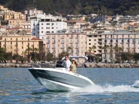 A couple enjoys a thrilling ride on a sleek boat, cruising through calm waters with a picturesque coastal backdrop — perfect for adventure seekers and romantic outings.