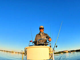 A man enjoys a day of fishing while steering a boat on calm waters, showcasing the perfect outdoor adventure for fishing enthusiasts.