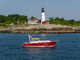 A vibrant red speedboat glides through the water near a picturesque lighthouse, showcasing the beauty of coastal boating adventures.