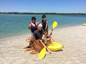 A joyful family poses on the beach with their golden retriever and kayaks, capturing a fun-filled day of kayaking and sun by the water.