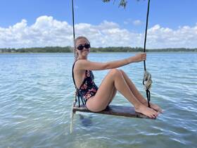 A young woman enjoys a sunny day swinging over the water, capturing the essence of fun and relaxation in a picturesque outdoor setting.