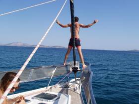 A man stands triumphantly at the bow of a sailboat, enjoying the ocean breeze and the thrill of sailing — a perfect moment of adventure on the water.