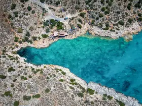 A stunning aerial view of a secluded cove with turquoise waters and rocky coastline, showcasing people enjoying the natural beauty of the area — perfect for beach lovers and nature enthusiasts.