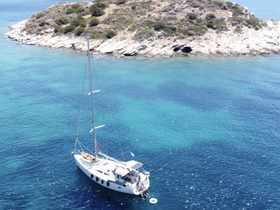 An aerial view of a sailboat anchored near a picturesque island, with guests enjoying the water — a perfect scene for summer adventures and island exploration.