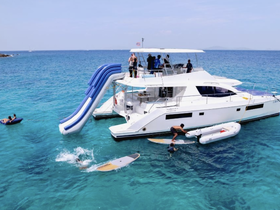 A lively scene featuring guests enjoying a water slide and paddleboarding off a luxurious catamaran, perfect for a fun-filled day on the water.
