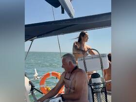 A group enjoys a sunny day sailing on the ocean, with one person steering the boat and others relaxing in the background — perfect for a fun day on the water.
