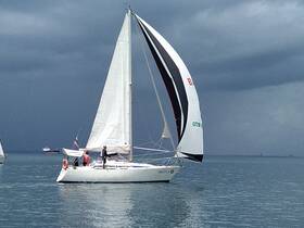 A sailboat gracefully navigates the waters with crew members on deck, showcasing the thrill of sailing amidst a dramatic sky.