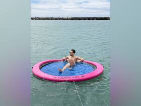 A man relaxes on a floating mat in clear waters, enjoying a beverage — the perfect way to unwind on a sunny day at the beach.
