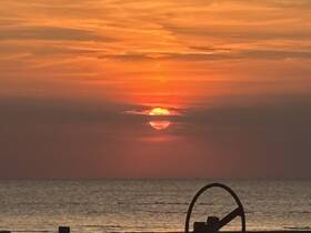 A stunning sunset over the ocean, framed by the silhouette of a boat's steering wheel, creating a picturesque scene perfect for evening cruises.