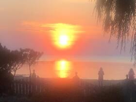 A stunning sunset casts vibrant colors over the water, with silhouettes of people enjoying the view from the beach — a perfect moment for relaxation and reflection.