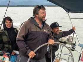 A lively group enjoys a sailing experience, with one person steering the boat while others share in the fun — perfect for adventure seekers on the water.