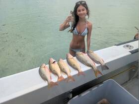 A young girl proudly holds a fish while showcasing a catch of the day on a boat, highlighting the excitement of fishing adventures.