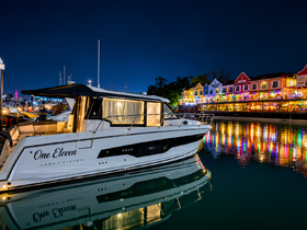 A beautifully lit Merry Fisher yacht named 'One Eleven' docked at night, reflecting the vibrant colors of nearby buildings in the water — a picturesque scene perfect for evening boat tours.