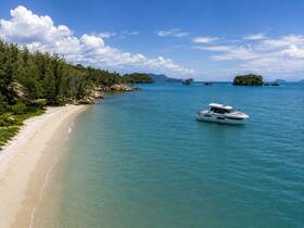 A stunning aerial view of a yacht anchored near a pristine beach, surrounded by clear turquoise waters and lush greenery — an ideal setting for a relaxing getaway.