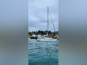 A serene view of a sailboat anchored near the dock, surrounded by calm waters and a picturesque hillside backdrop.