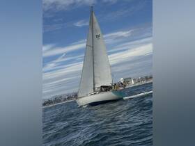 A beautiful sailboat glides through the waves, showcasing its elegant design against a backdrop of blue skies and coastal scenery.