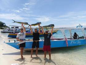 Three friends proudly display their catch after a successful fishing trip, with the 'Blue Sky' boat in the background, capturing the joy of a day on the water.