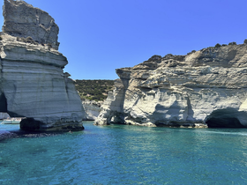 Stunning view of unique rock formations along the coastline, with a glimpse of a swimmer enjoying the crystal-clear waters — a perfect destination for island exploration.