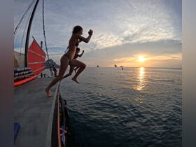 A group of friends joyfully jumps off the side of a boat into the water at sunset, capturing the essence of adventure and fun on the water.