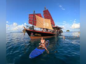 A vibrant scene featuring a woman paddleboarding alongside a traditional boat, with guests enjoying the water — perfect for island hopping adventures.